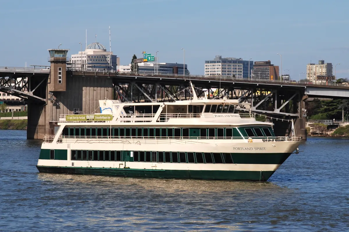 A cream-and-green Portland Spirit cruise boat on the Willamette River in front of the Morrison Bridge