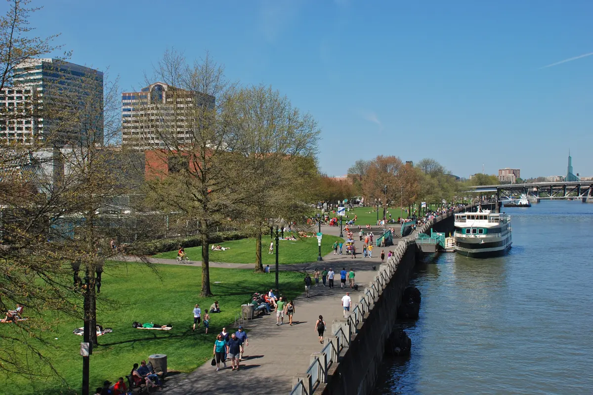 Walkers and picnickers on the lawns and seawall path of Tom McCall Waterfront Park, with a cruise boat moored at the dock