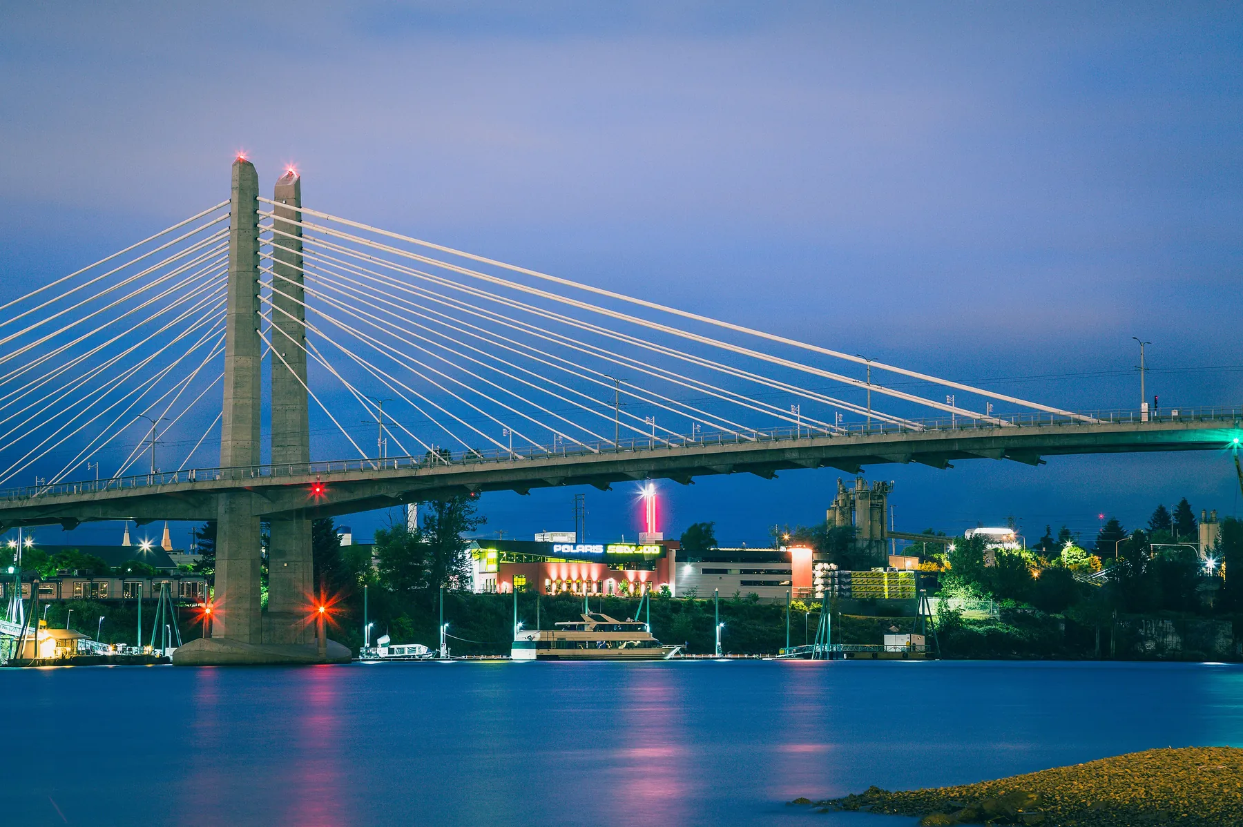 Tilikum Crossing's white cable-stayed towers against a blue-hour sky, with a tour boat moored beneath the span